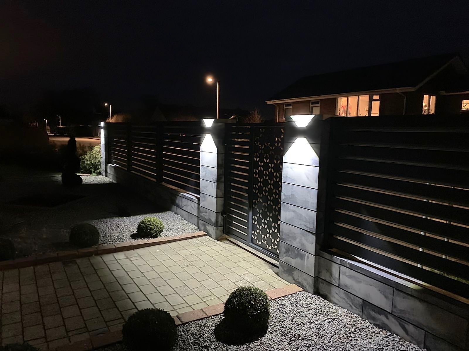 Modernios skardinės tvoros su LED apšvietimu stulpuose, sutemų metu