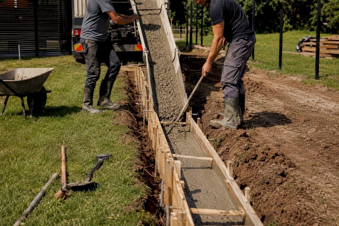 Šviežias betonas pilamas į tvoros pamatų tranšėją